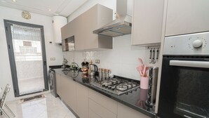 Una cucina moderna con piano cottura in acciaio inossidabile, forno integrato e cappa aspirante. Si nota un lavello e una finestra con porta in vetro acidato.