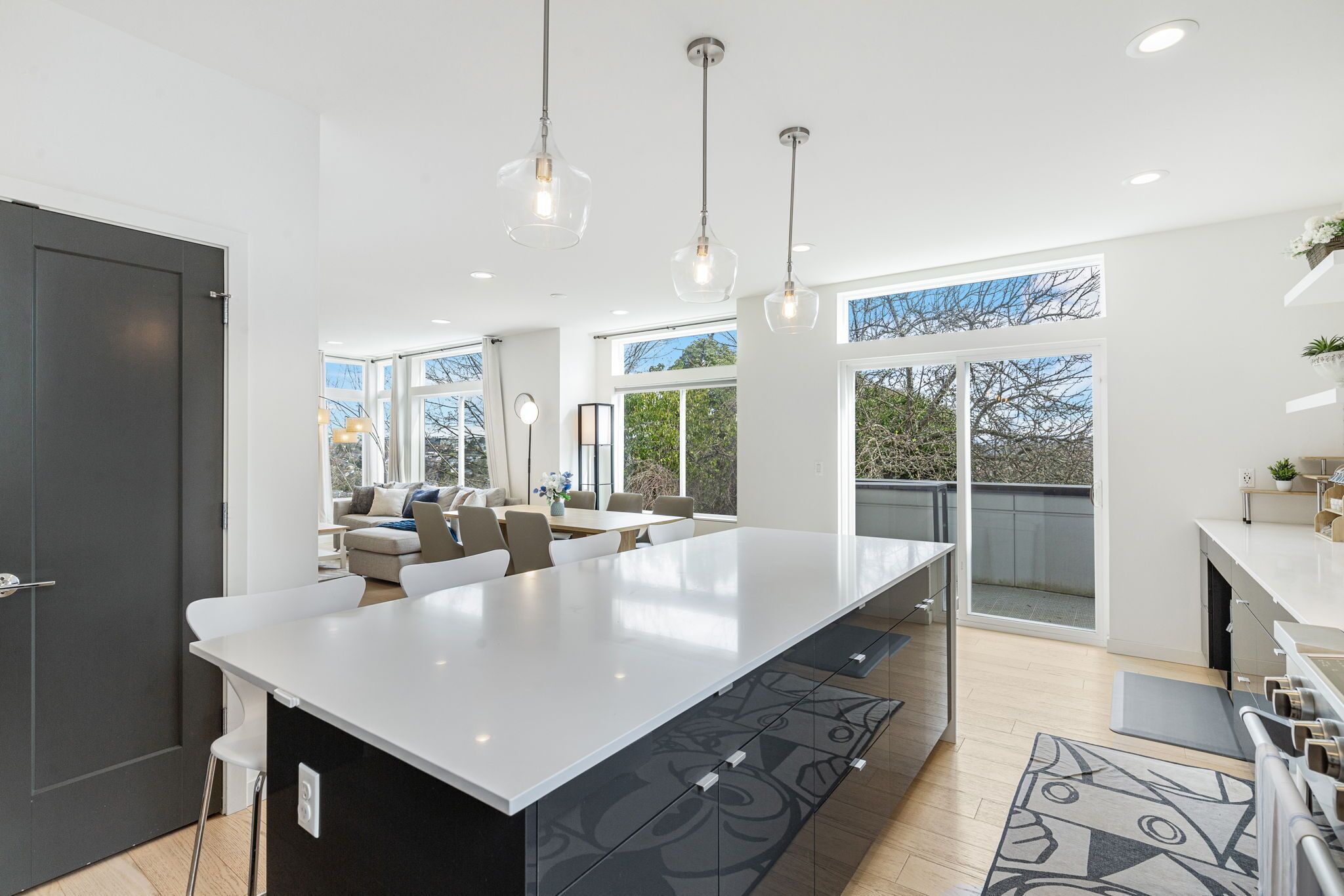 A modern kitchen with a large island, pendant lighting, and a view to an outdoor balcony.