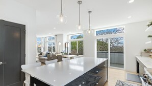 Une cuisine moderne dotée d’un grand îlot central, de luminaires suspendus et donnant sur un balcon extérieur.