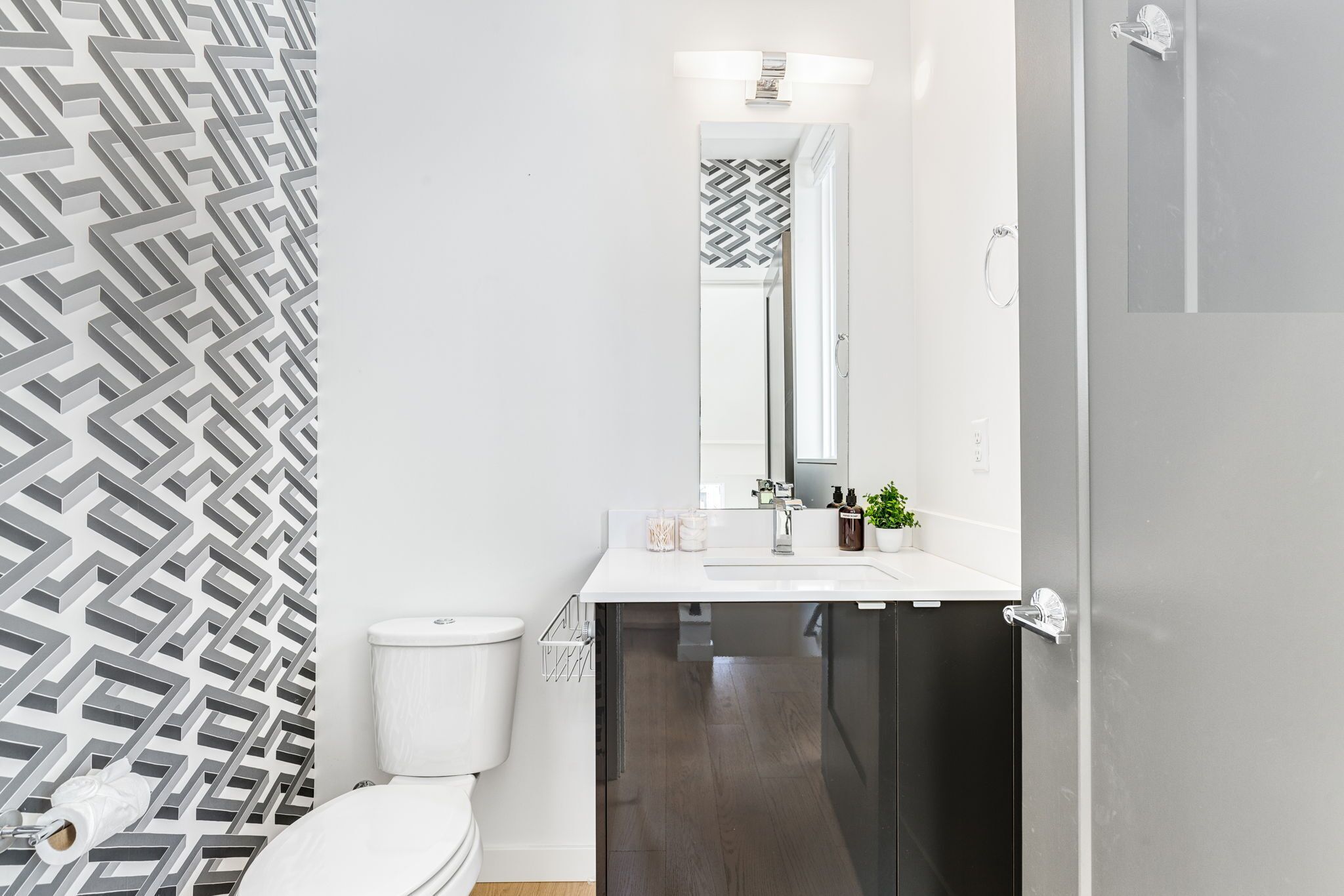 Un baño moderno con inodoro blanco, lavamanos negro y espejo encima.