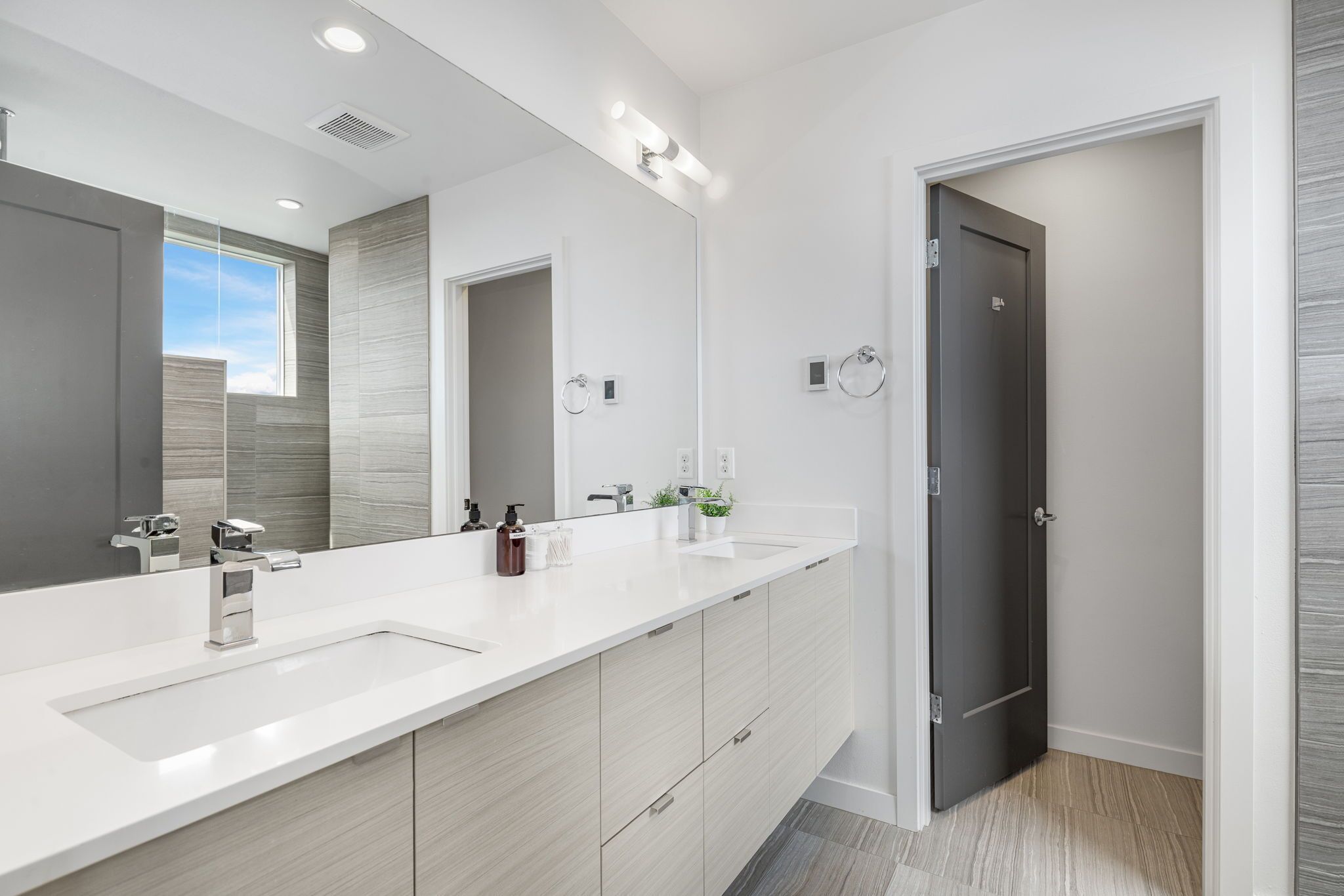 A modern bathroom with a large mirror, two sinks, and a dark door.