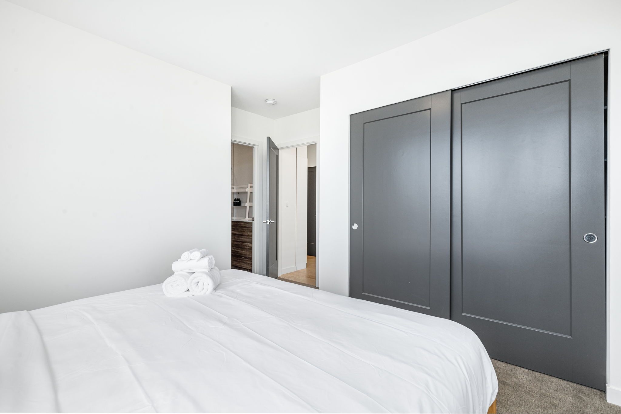 Een hotelkamer met een net opgemaakt bed, een garderobe met twee deuren en een zichtbare kast op de achtergrond.