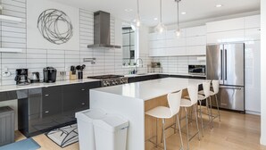 Une cuisine moderne dotée d’un grand îlot central, d’appareils électroménagers en acier inoxydable et de luminaires suspendus.