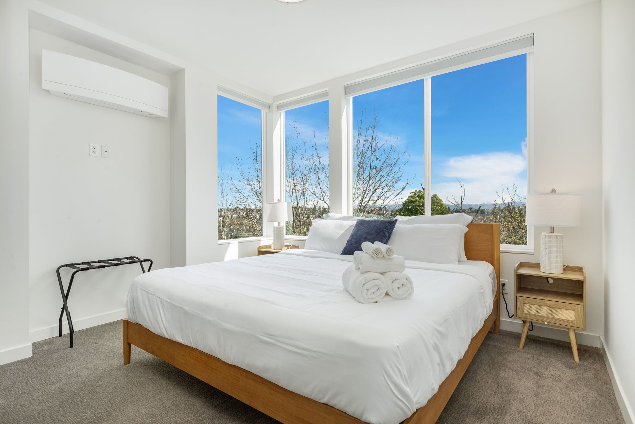 Une chambre moderne avec un grand lit, une table de chevet, une commode et une fenêtre donnant sur des arbres et des montagnes.