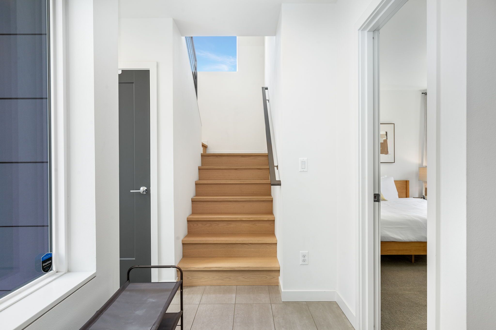 Una escalera que lleva a un dormitorio con una cama, un ventanal y una puerta.