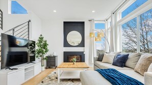 Un salon moderne avec un téléviseur, une cheminée, un canapé et de grandes fenêtres.