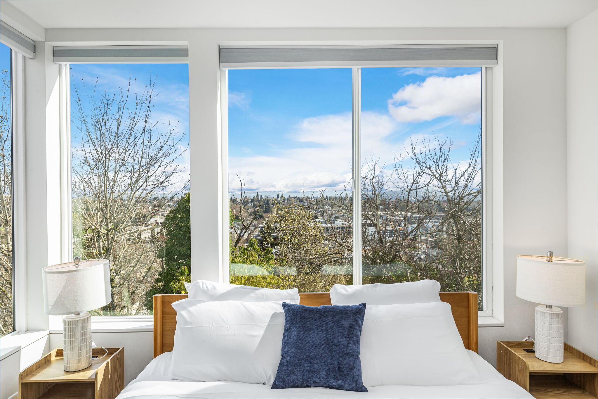 Ein Schlafzimmer mit großem Fenster, einem Bett mit weißen und blauen Kissen und zwei Nachttischen mit Lampen.