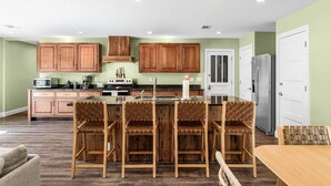 Une cuisine avec des meubles de rangement en bois, un îlot central doté de tabourets, et un réfrigérateur.