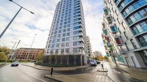 En moderne højhusbygning med en buet facade, flere altaner og en parkeringsplads foran.