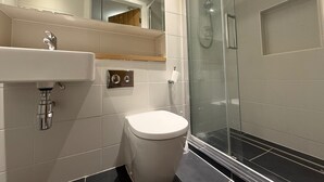 Et moderne badeværelse med en glasafskærmet bruseniche, et hvidt håndvask og et toilet.