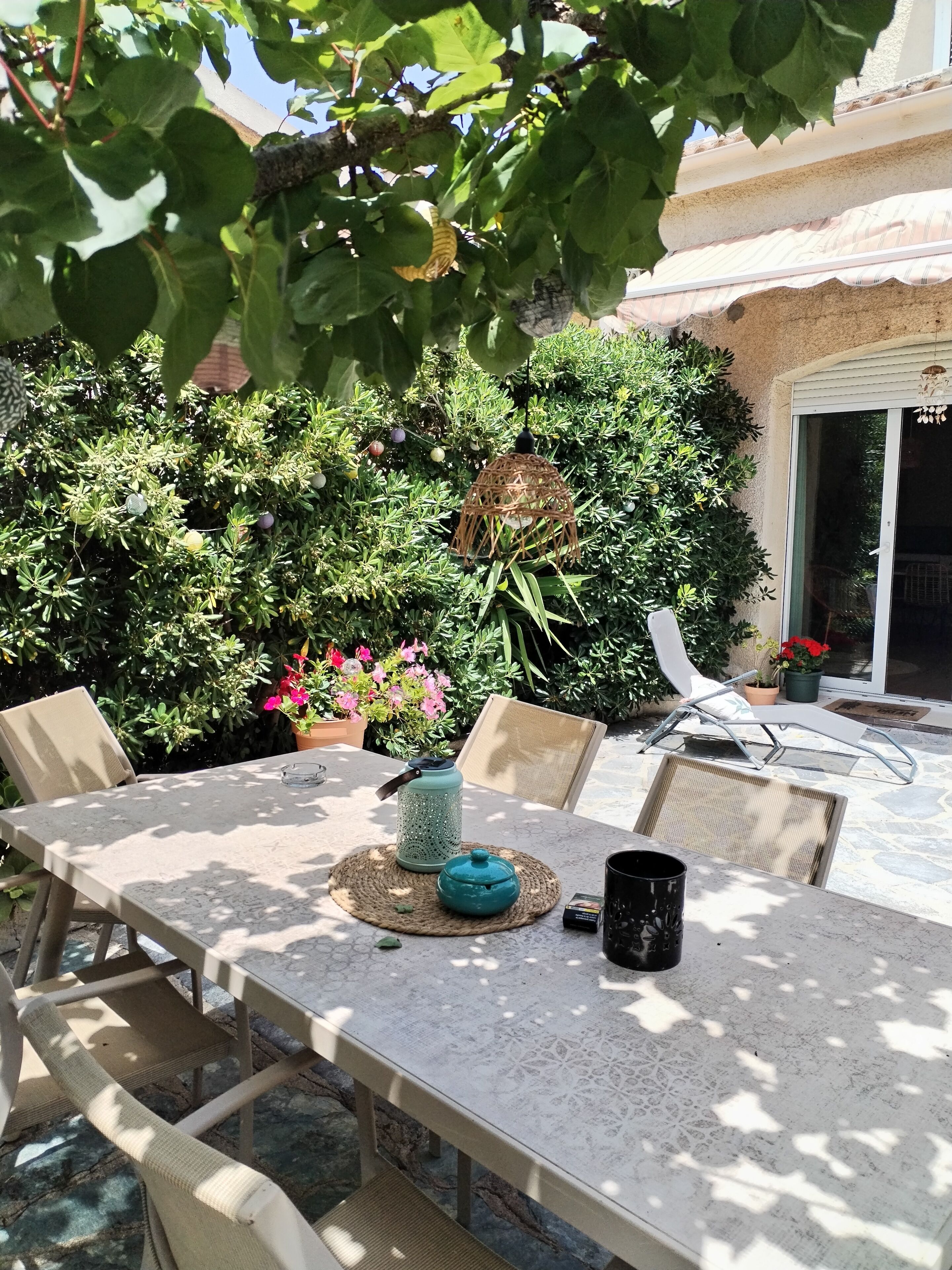 Un patio al aire libre con una mesa dispuesta para comer, rodeado de abundante vegetación y plantas en macetas.
