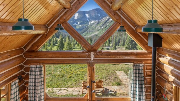 A log cabin with a triangular window offering a mountain view.
