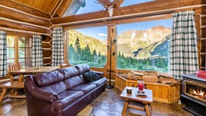 A log cabin interior with a leather sofa, wooden dining table, and a stone fireplace.