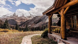 A wooden cabin with a stone pathway leading to a porch overlooking a mountainous landscape.