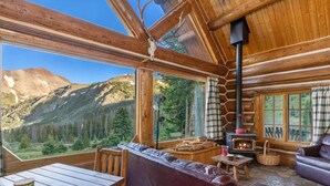 A log cabin with a stone fireplace, leather sofa, wooden table, and a view of mountains.