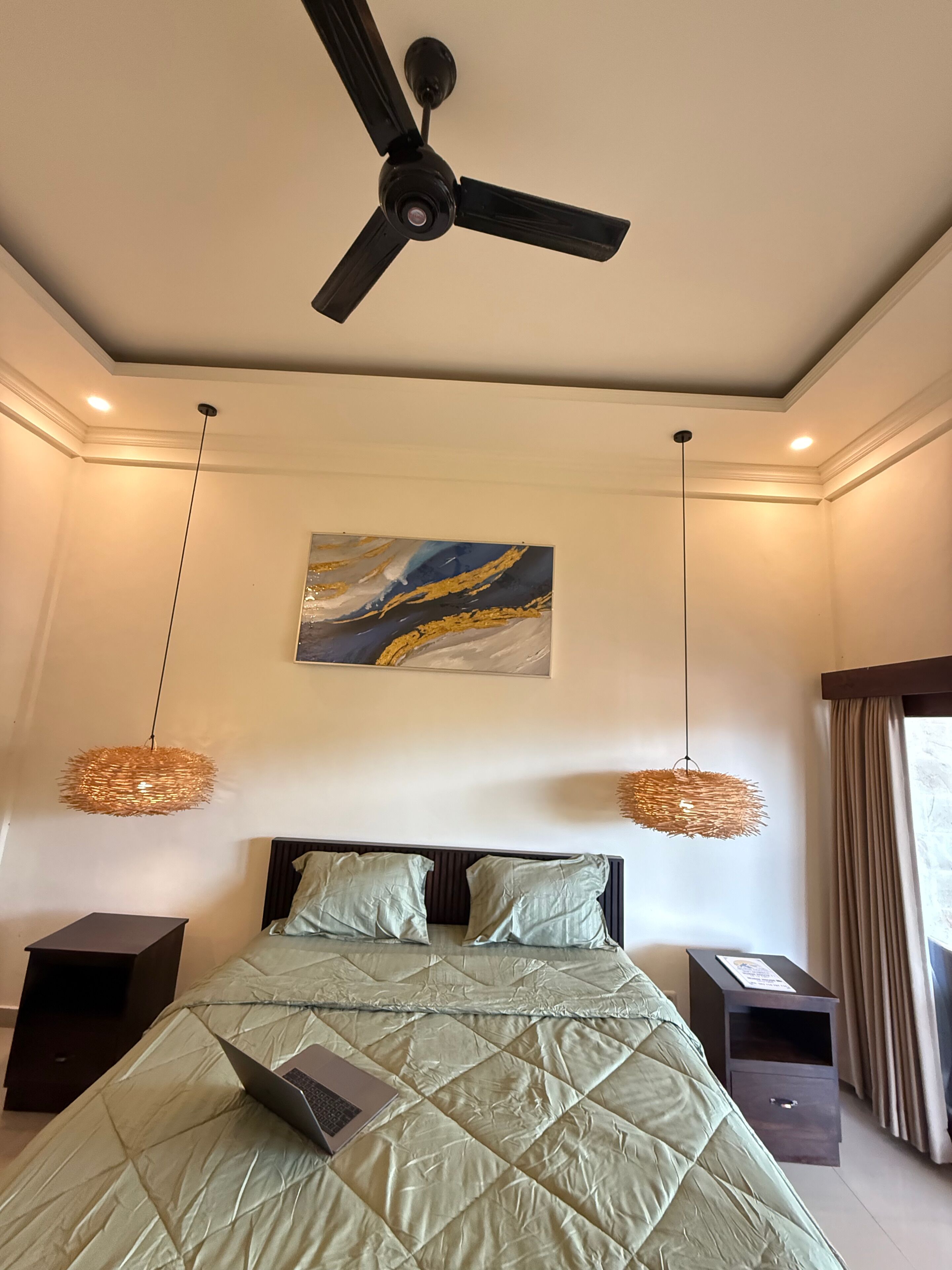 A bedroom with a bed, ceiling fan, artwork, and two bedside tables.