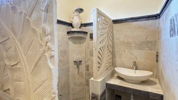 A bathroom with a large decorative stone archway, a freestanding sink, and a shower with a stone wall.