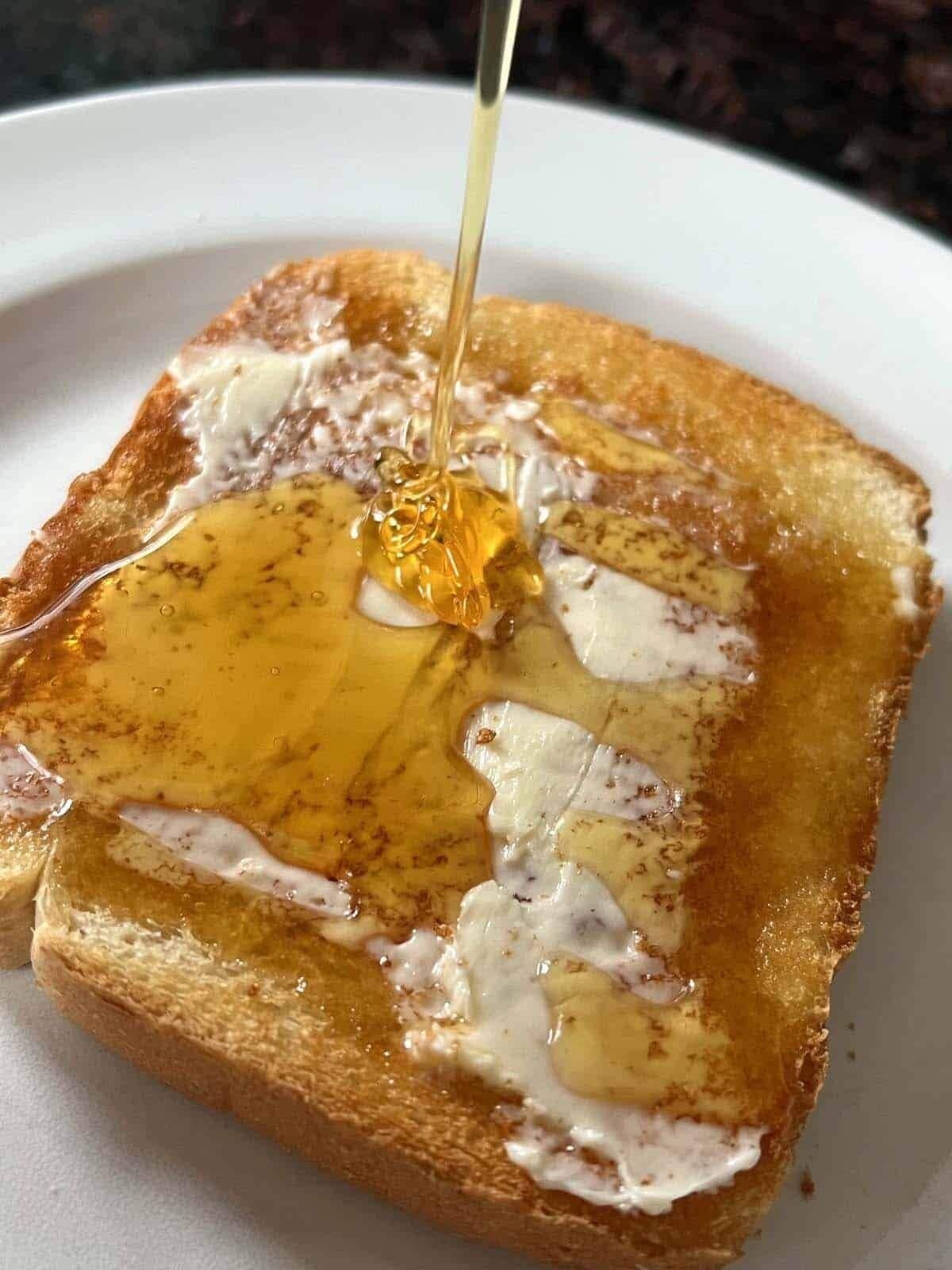 A slice of toast with butter and honey being poured on it.