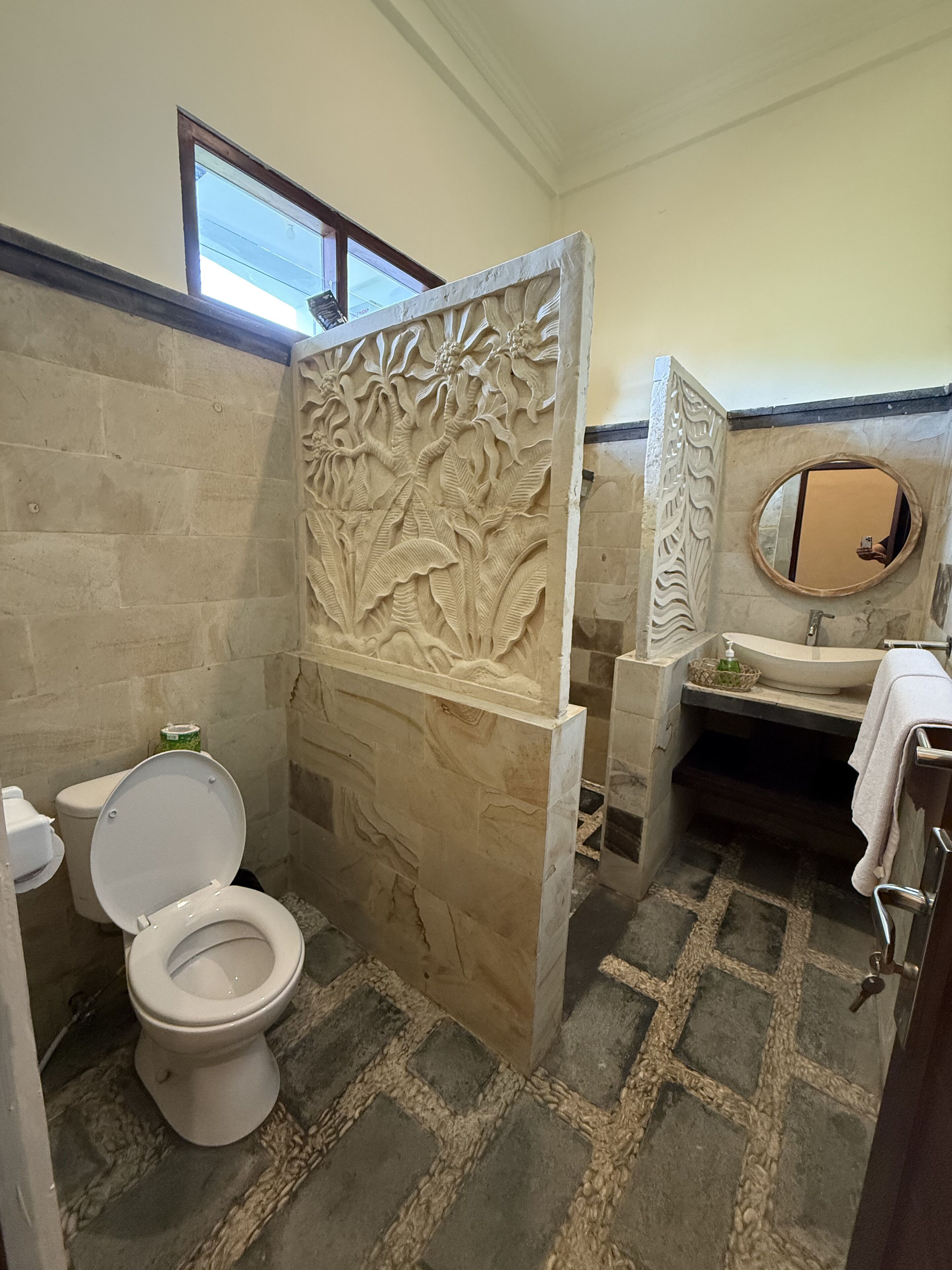 A bathroom with a stone floor, a toilet, a sink, and a decorative panel with floral carvings.