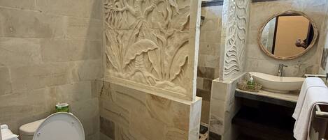 A bathroom with a stone floor, a toilet, a sink, and a decorative panel with floral carvings.