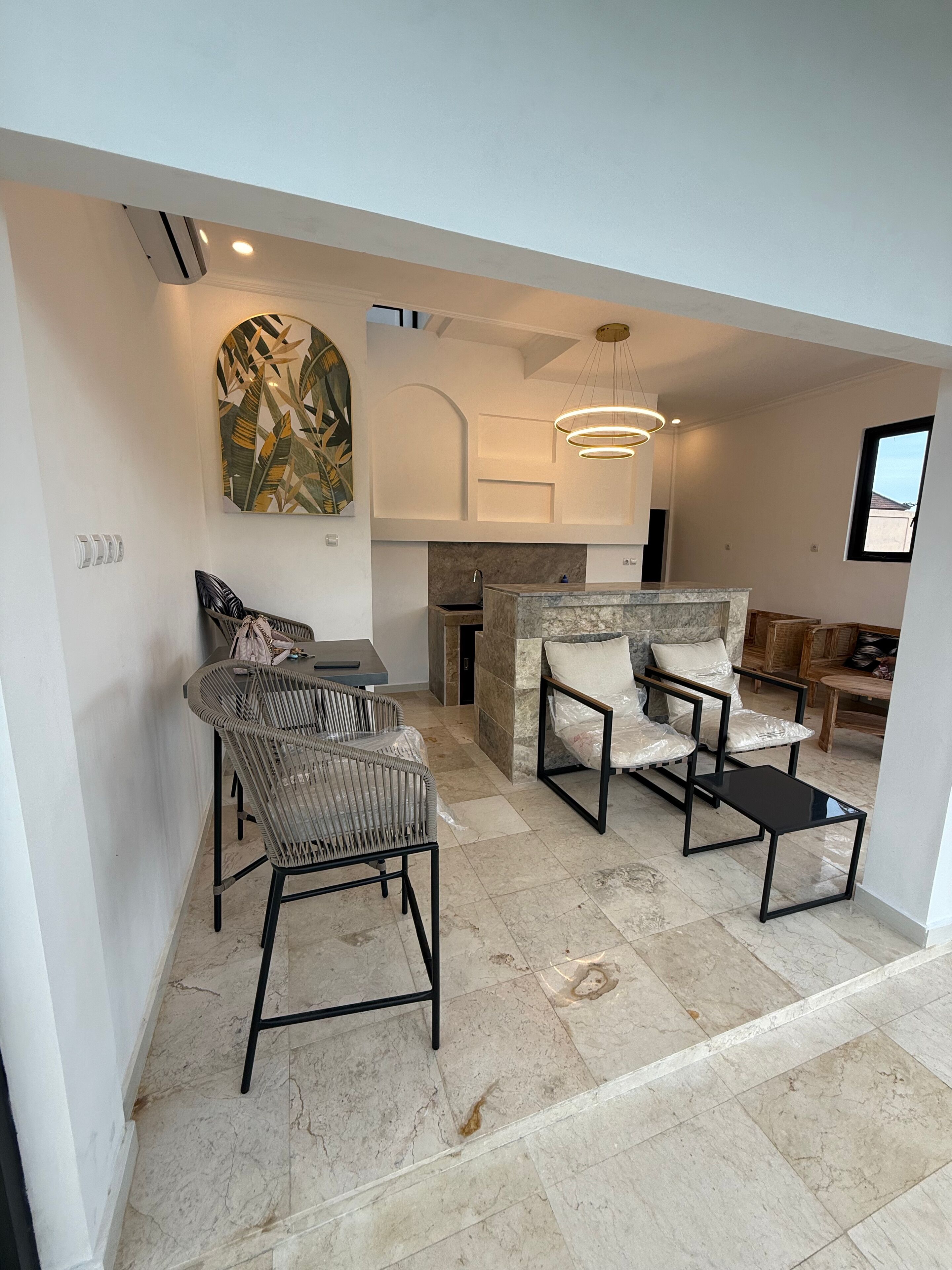 Eine moderne Küche mit Marmorarbeitsplatte, ein Essbereich mit Korbstühlen und ein Wohnbereich mit Sofa und Fernseher.