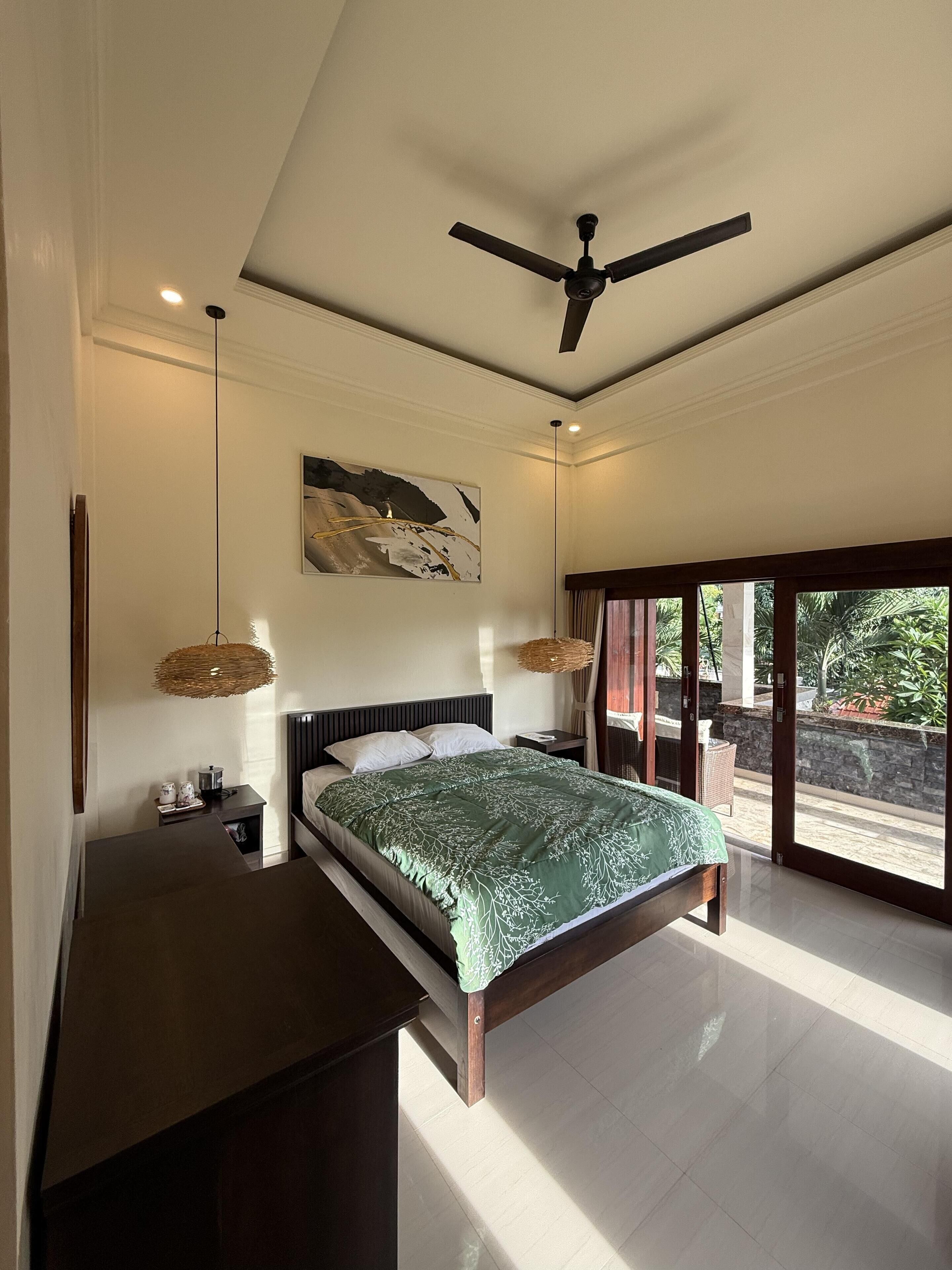 A spacious bedroom with a large bed, a ceiling fan, and a view of the outdoors through large windows.