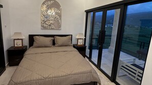 A bedroom with a large bed, a ceiling light fixture, a wall-mounted abstract art piece, and a balcony with a view. - Murni's House (Buleleng)