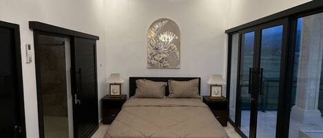 A bedroom with a large bed, a chandelier, a wall-mounted artwork, and a balcony door.