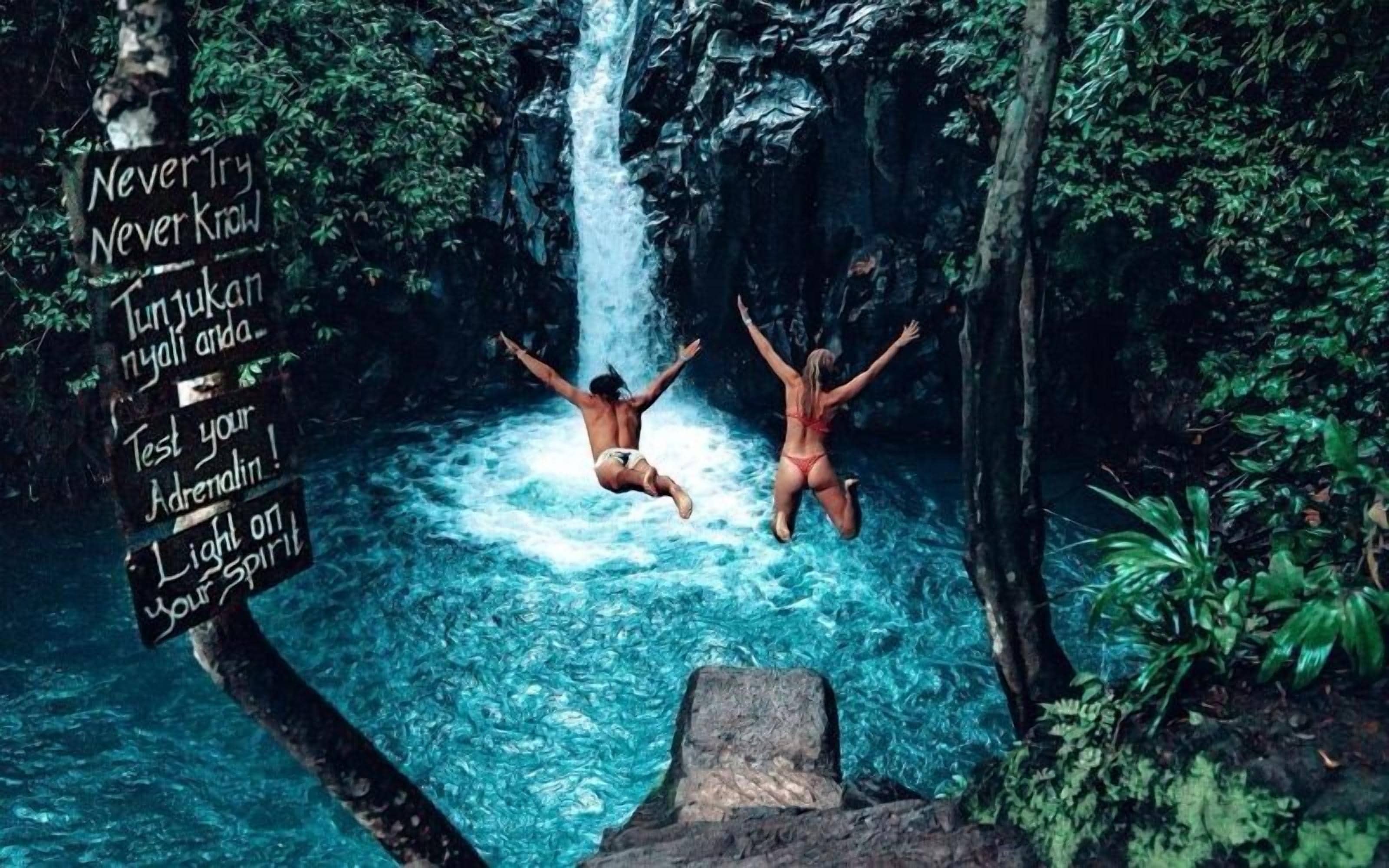 A person jumping off a cliff into a waterfall surrounded by greenery.