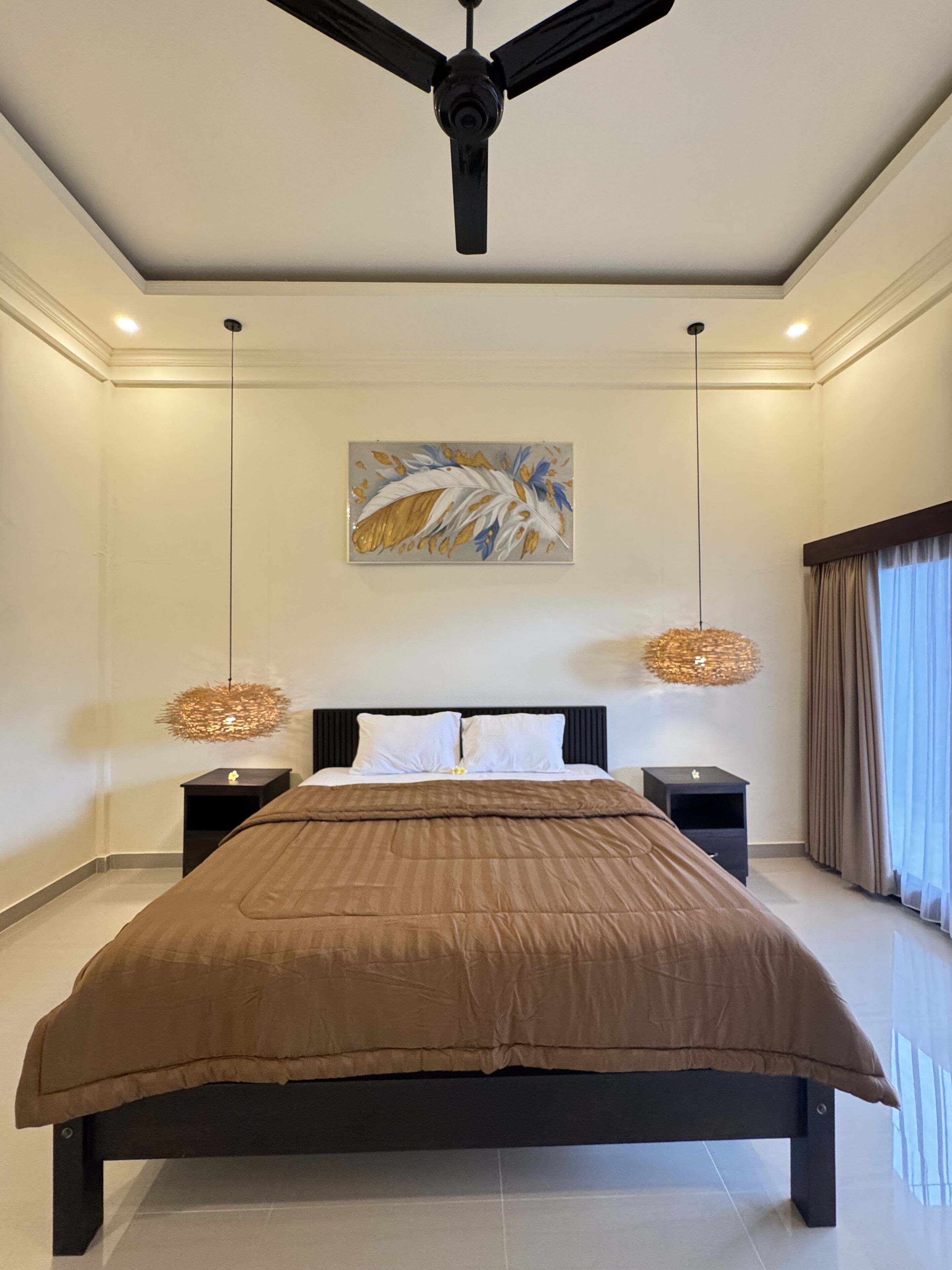 A modern bedroom with a large bed, a ceiling fan, two bedside lamps, and a decorative wall piece.