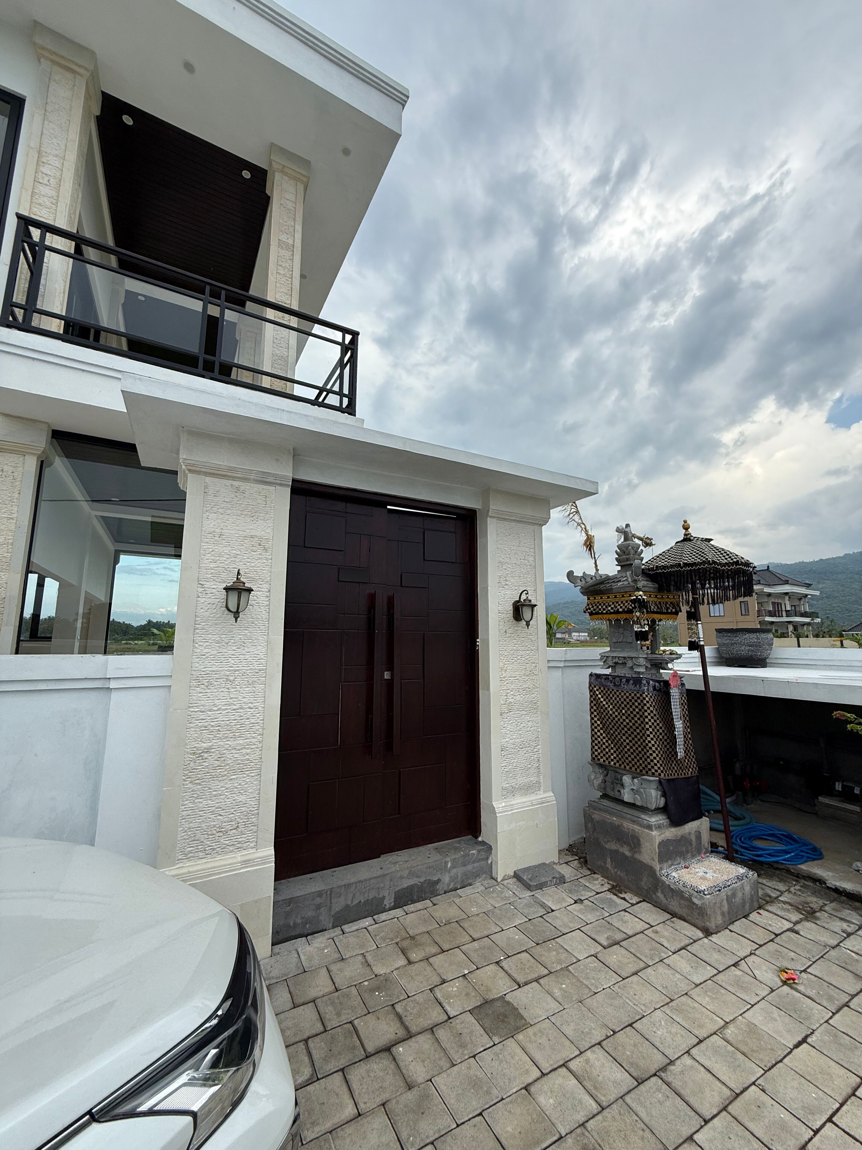 A modern two-story building with a dark brown gate, white textured walls, and a balcony.