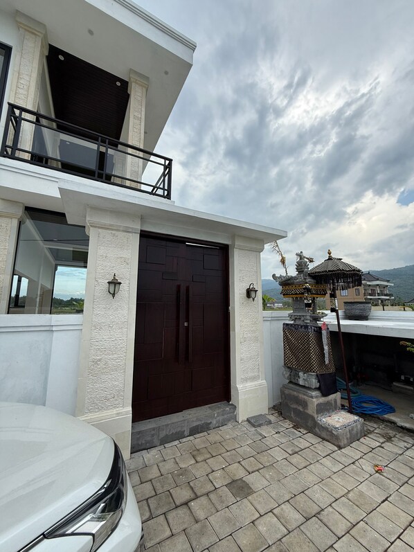 A modern two-story building with a dark brown gate, white textured walls, and a balcony. - Murni's House (Buleleng)