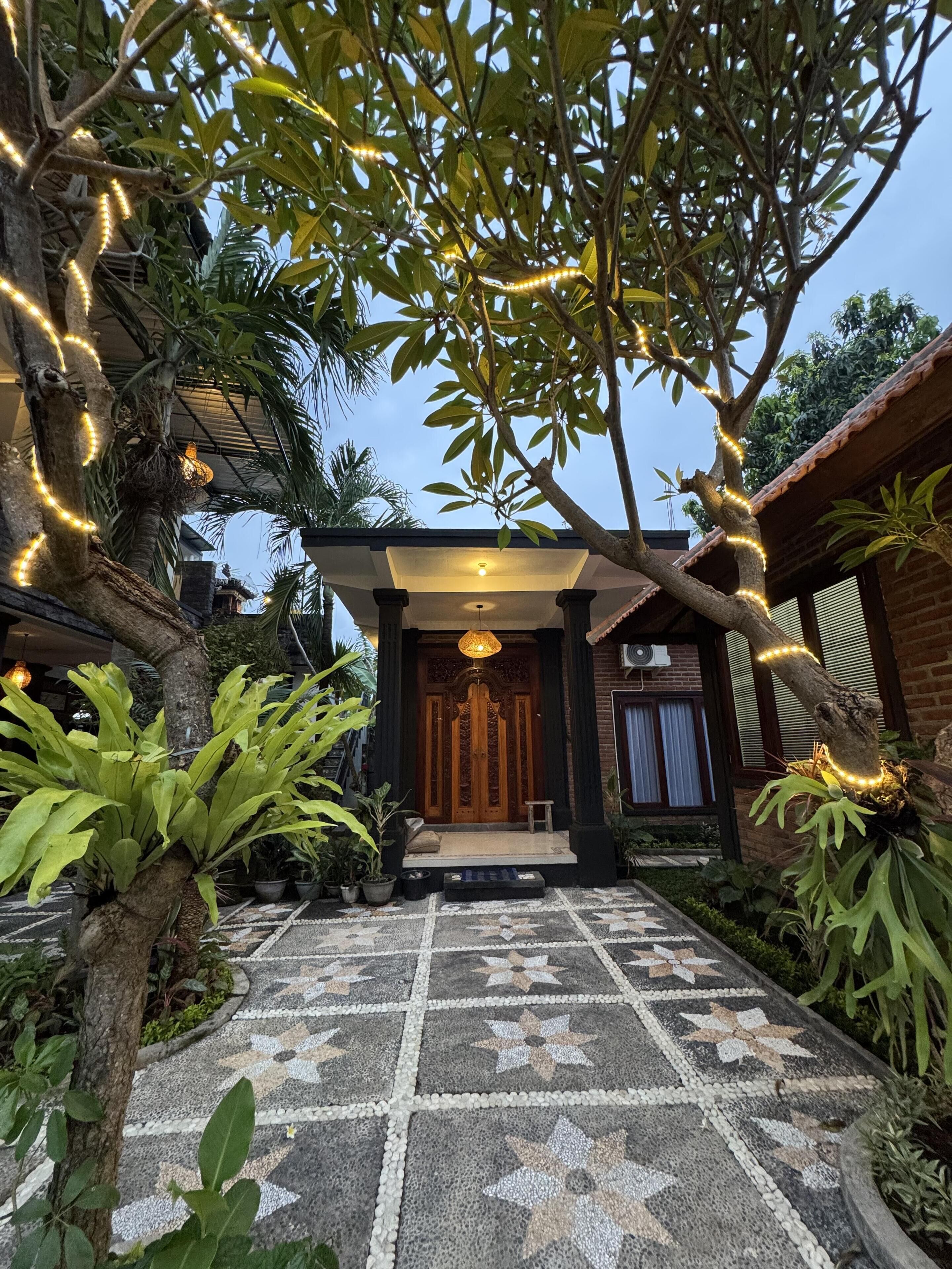 A house with a tiled entrance, surrounded by lush greenery and decorative lights.
