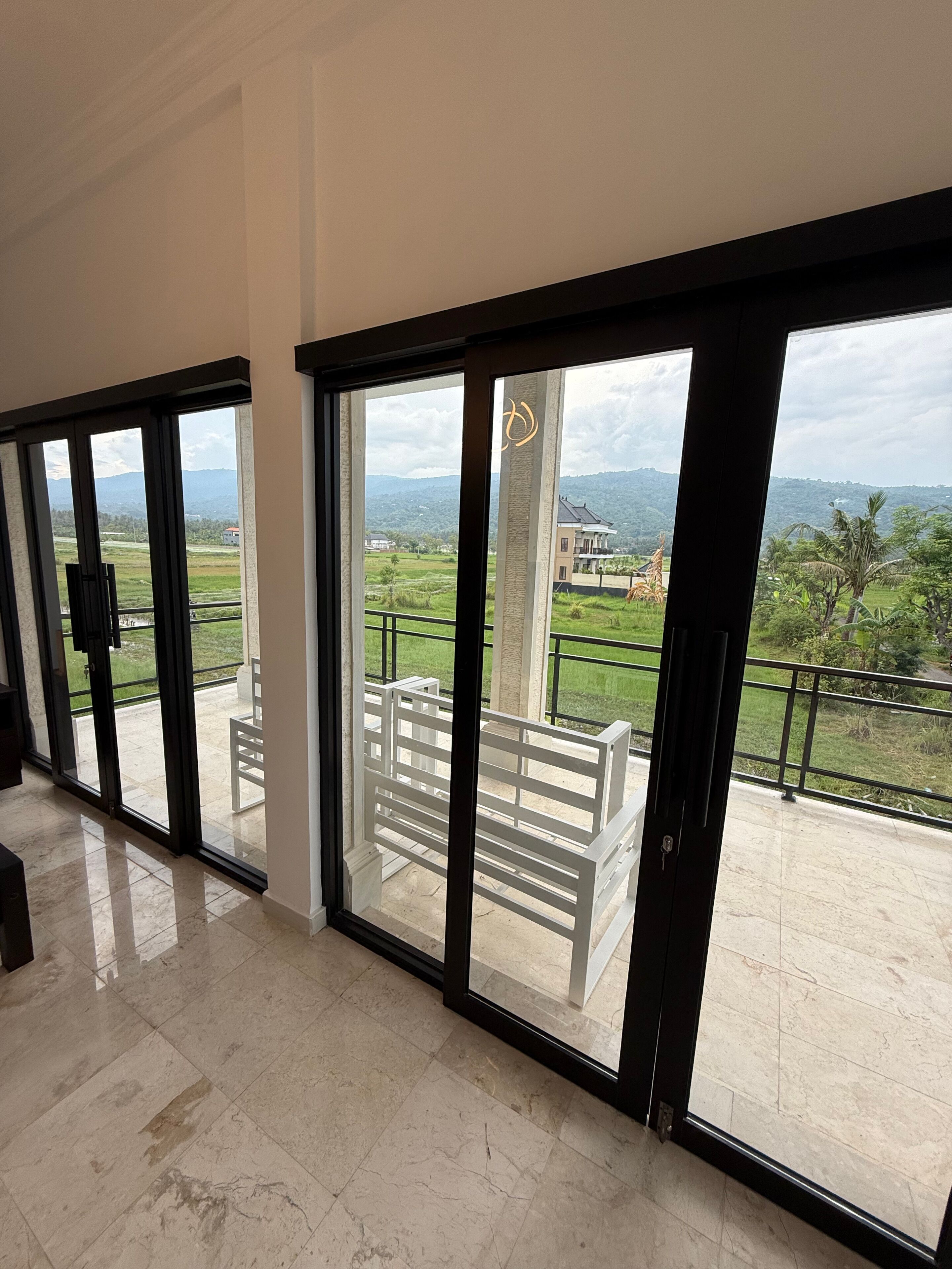 A spacious room with large sliding glass doors leading to a balcony with a white railing and a view of a green landscape.