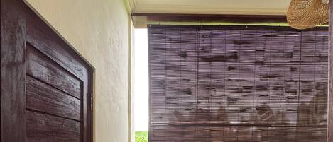 Un pasillo estrecho con una puerta de madera oscura a la izquierda, una ventana con persianas horizontales y un pequeño mostrador a la derecha.