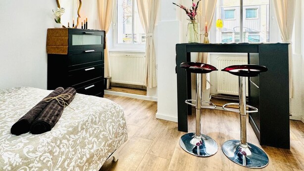 Een hotelkamer met een bed, een bureau met twee krukken, een spiegel en een raam met gordijnen.