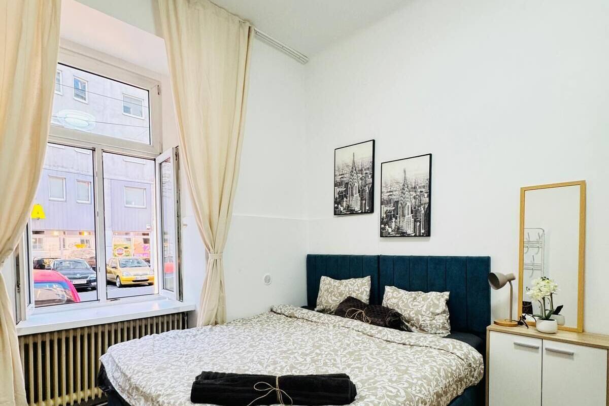 Een netjes ingerichte slaapkamer met een groot bed, een nachtkastje met spiegel, en twee ingelijste foto’s aan de muur.