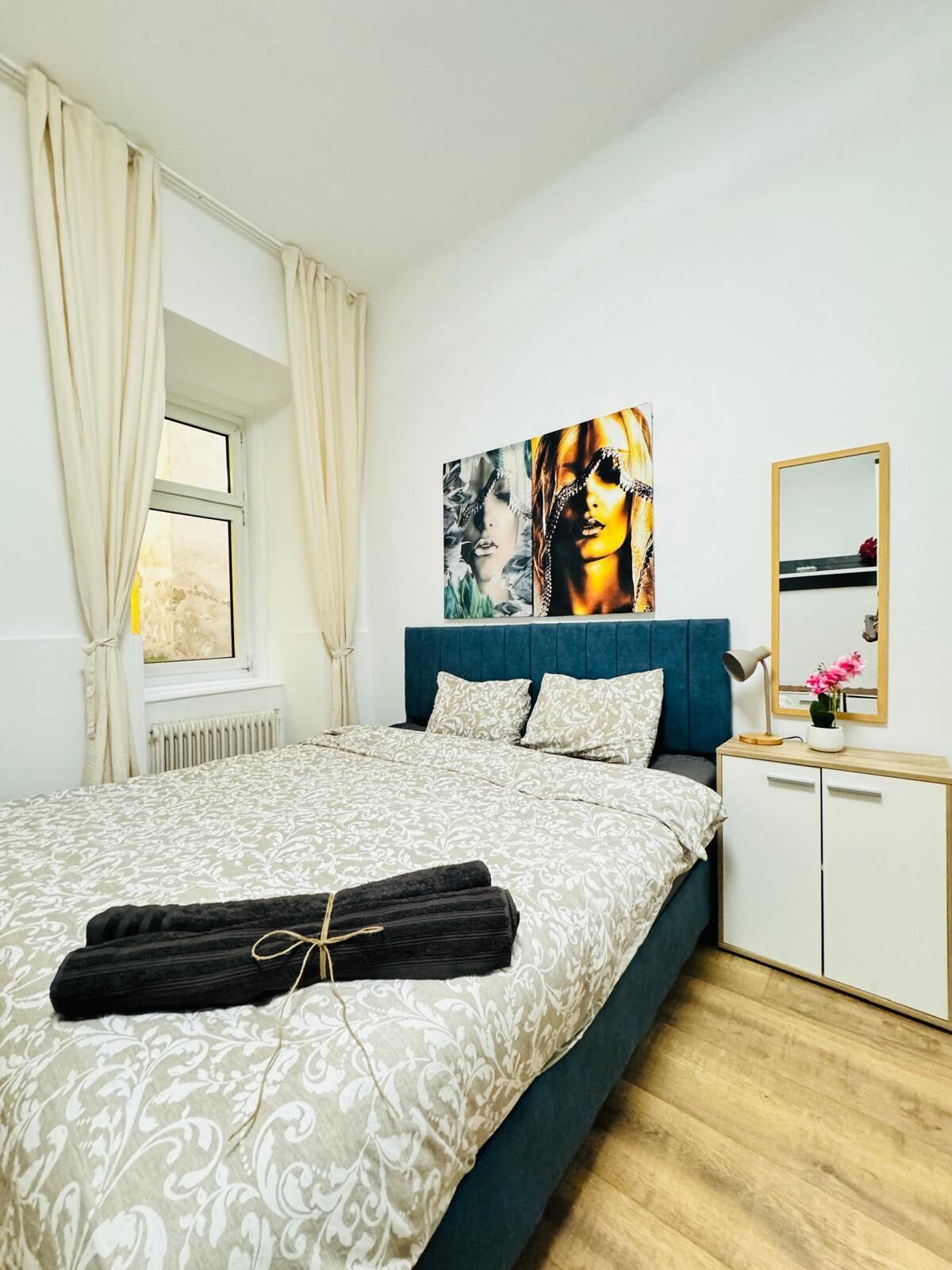 Una camera da letto con un letto, una testiera, una finestra con tende, un comodino con una lampada e un armadio.
