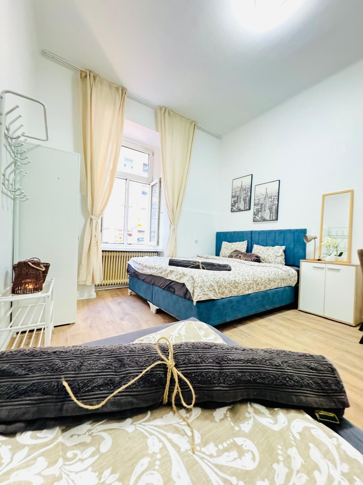 Een slaapkamer met een bed, een dressoir, een radiator en een raam met gordijnen.