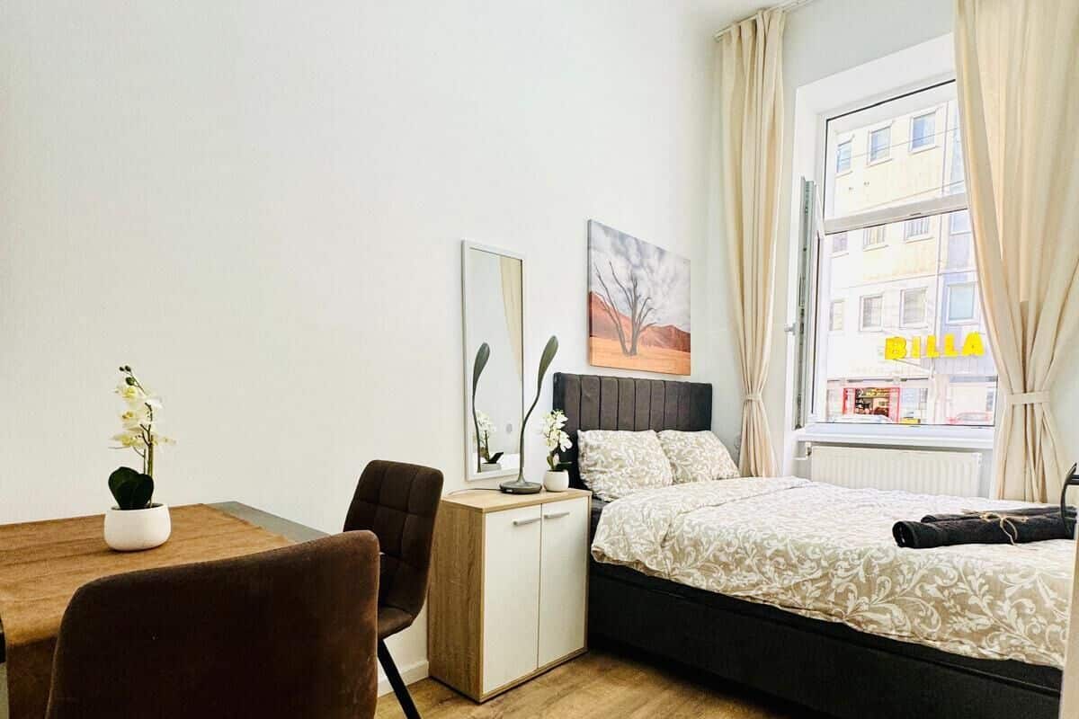 Een kleine slaapkamer met een bed, een bureau, een stoel en een raam met gordijnen.