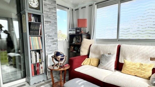 A cozy living room with a red sofa, a bookshelf, a globe on a small table, and a large window with a view.