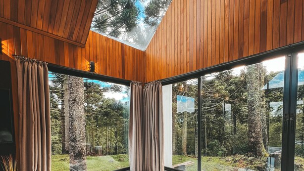A modern bathroom with a large bathtub, wooden flooring, and large windows offering a view of the outdoors.