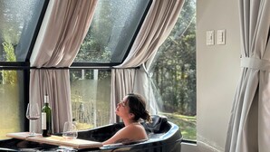 A spa tub by a large window with curtains, a wine bottle, and glasses on a tray.