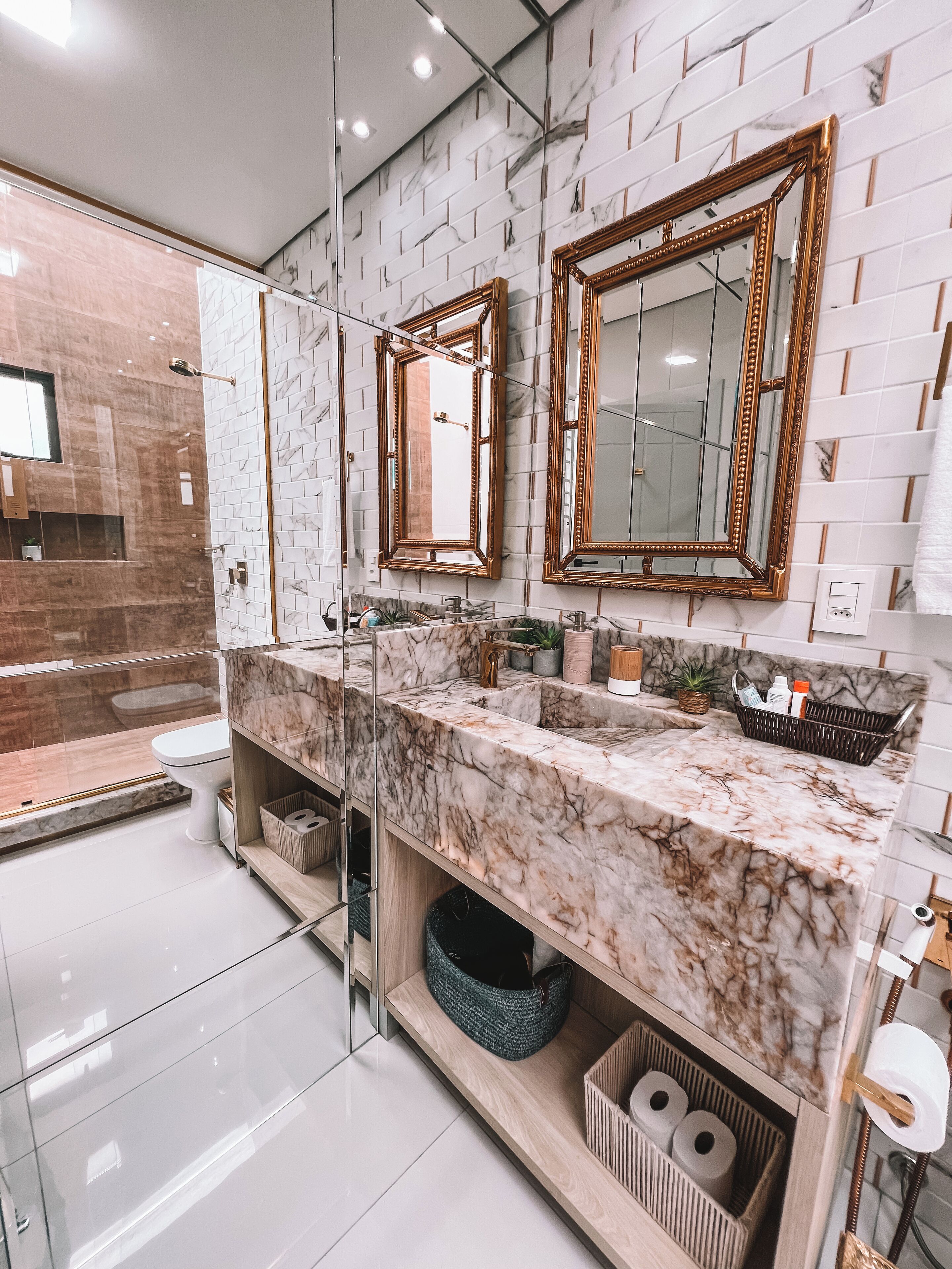 A modern bathroom with marble countertops, two large mirrors, and a glass-enclosed shower area.