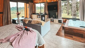 A spacious room with a large bed, a seating area, and a hot tub.