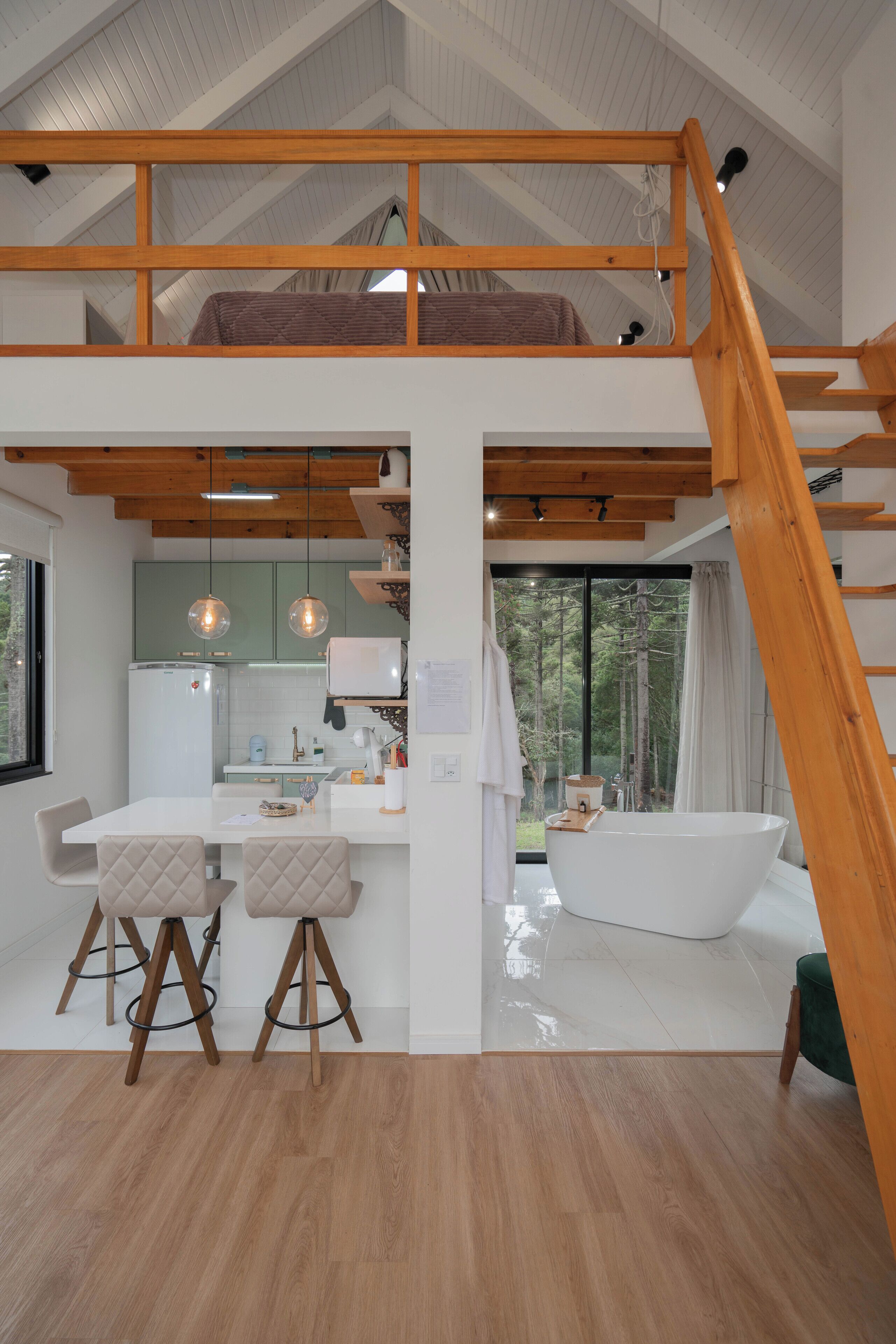 A modern kitchen with a central island, wooden beams, and a large window overlooking a forest.
