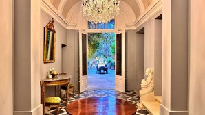 A grand hallway with a checkered floor, a round table, a chandelier, and a view of an outdoor garden. - Palazzo dei Fiori since 1883 (Balzan)