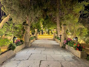 A stone pathway leading through a garden with a fountain at the end.