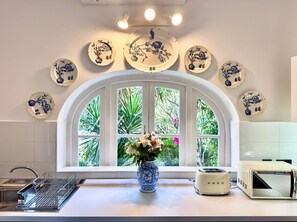 A kitchen with a white countertop, a dish rack, a toaster, and a window with a view of greenery. - Palazzo dei Fiori since 1883 (Balzan)