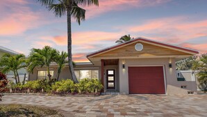A modern house with a red garage door, a paved driveway, and a well-maintained garden with palm trees and shrubs.